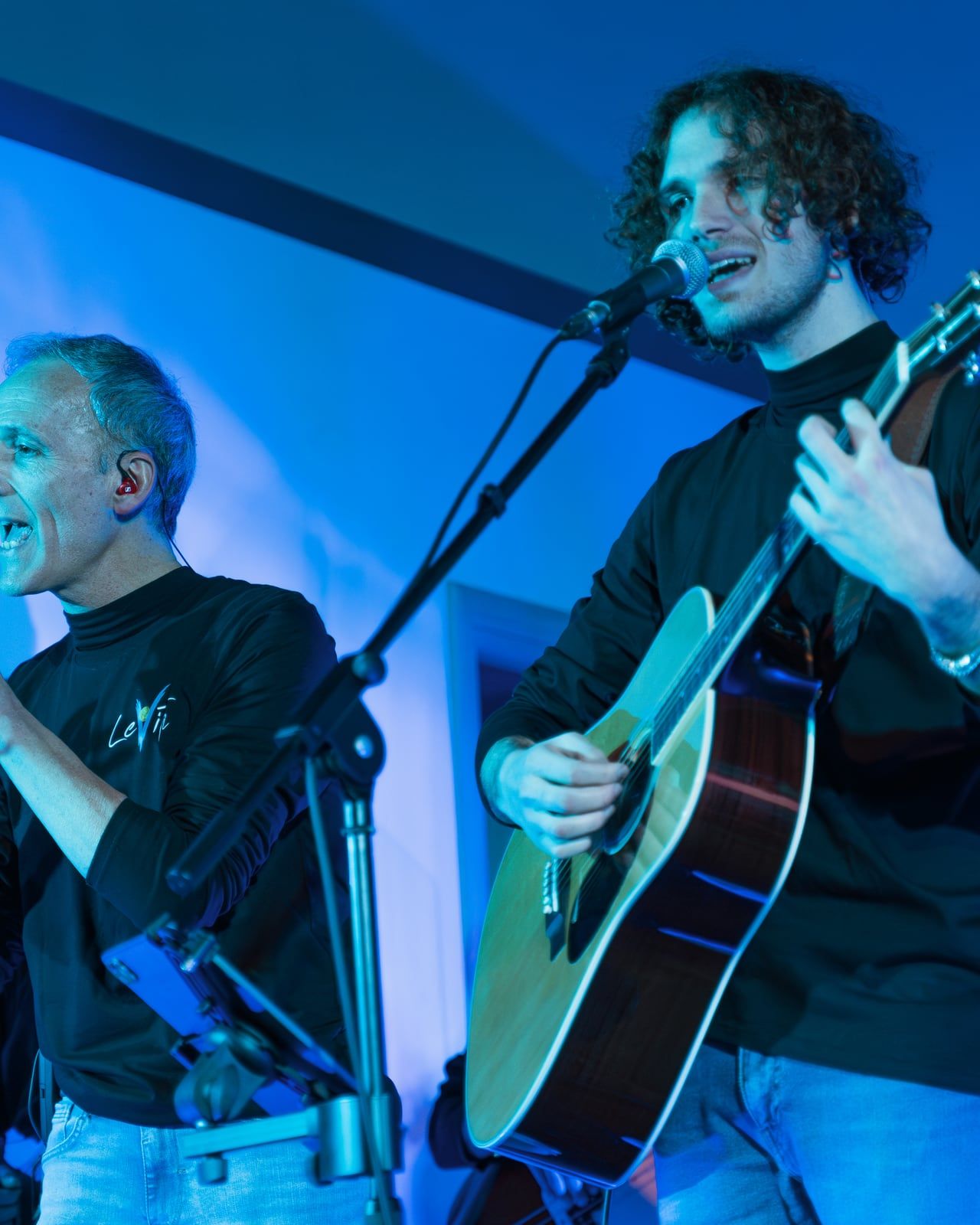 Un cantante e un chitarrista acustico sotto una luce blu