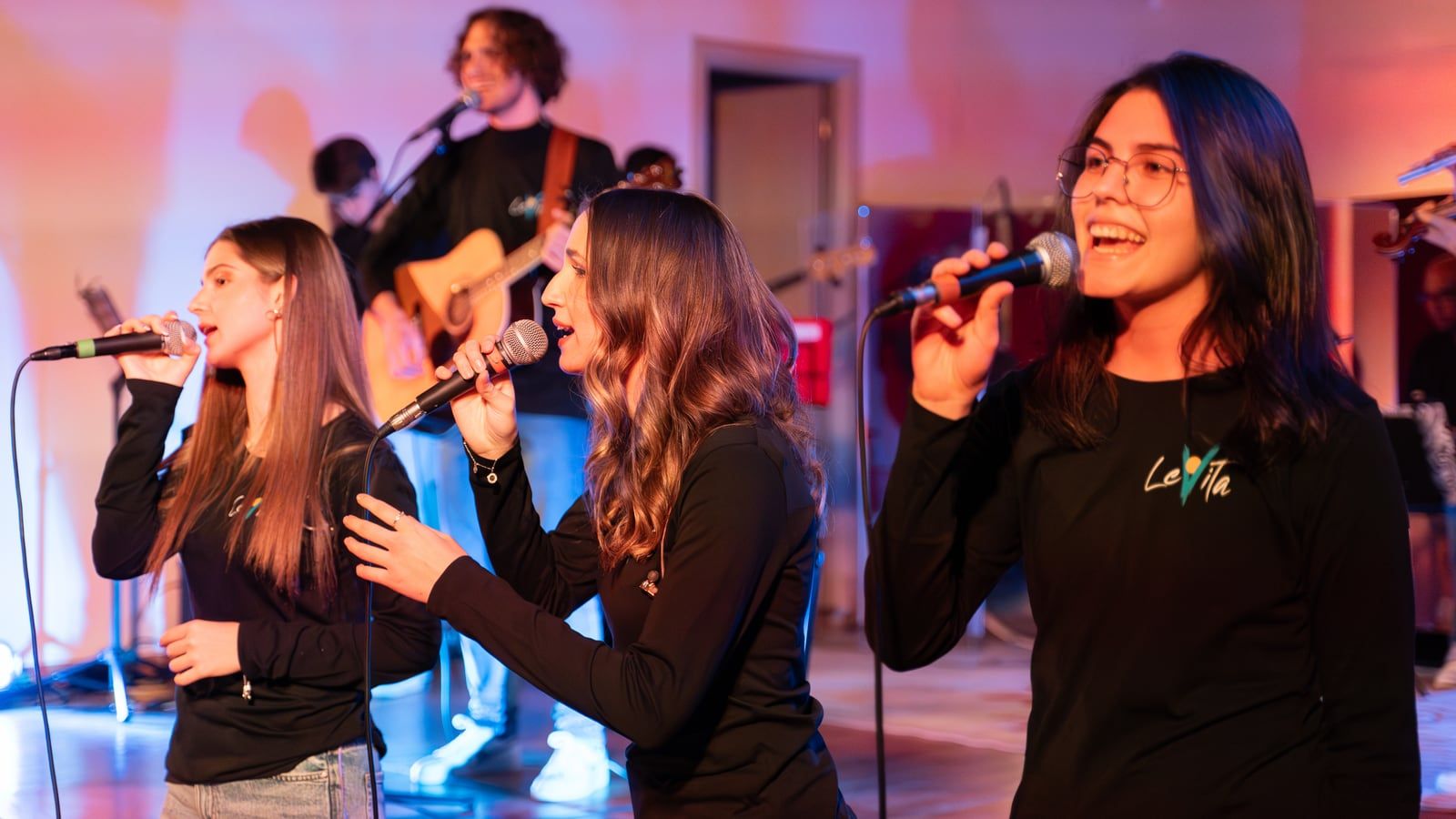 Le coriste cantano sorridendo, con la band alle spalle